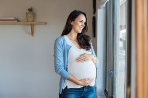 happy pregnant woman looking out window